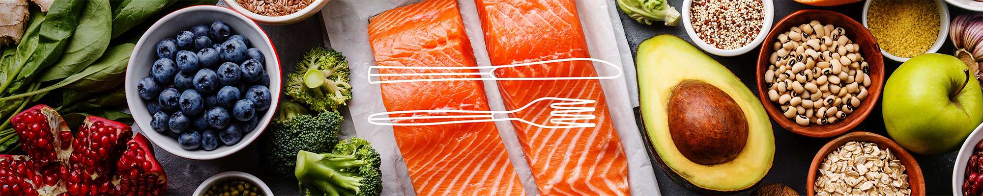 Ingredients on a granite table, including raw salmon fillets, fresh vegetables, fruit and beans